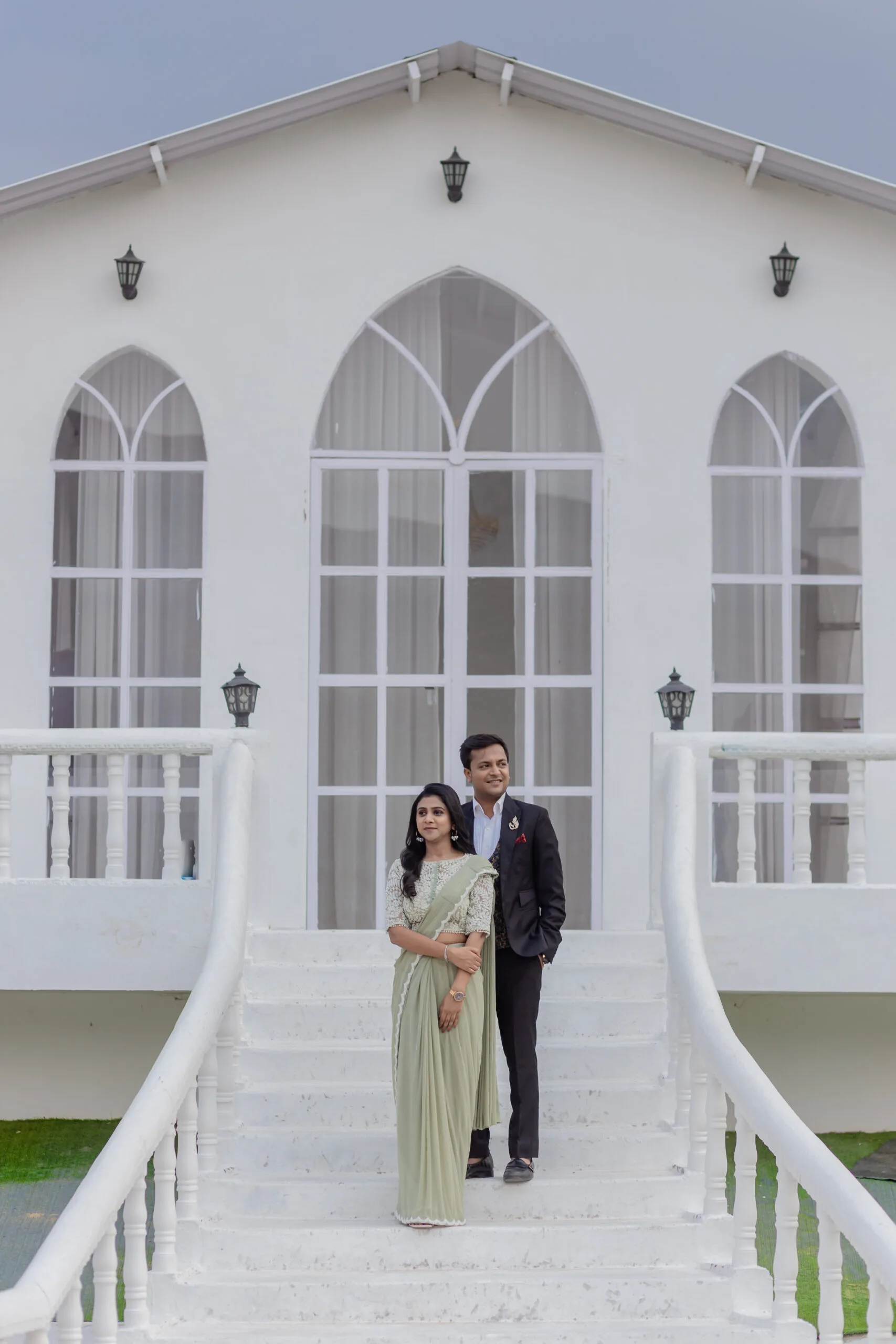 A couple in a saree and suit posing on white stairs in front of a modern building for their Pre Wedding Shoot in Jaipur.